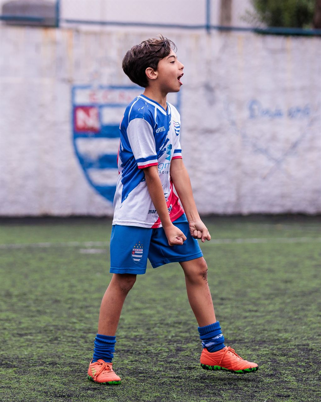 Aluno do Nacional comemorando em campo, com o escudo do clube pintado no muro ao fundo